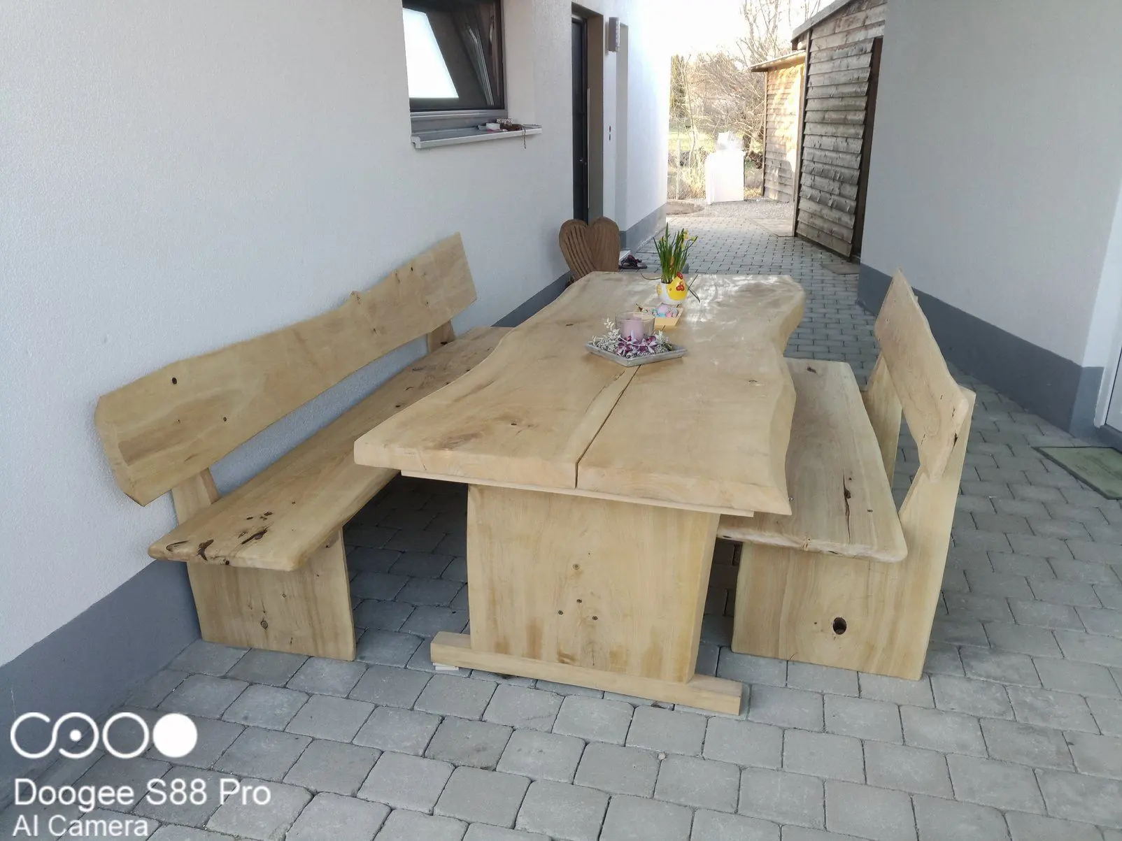 Massive Gartengarnitur aus Holz mit Tisch und zwei Bänken vor einem Haus